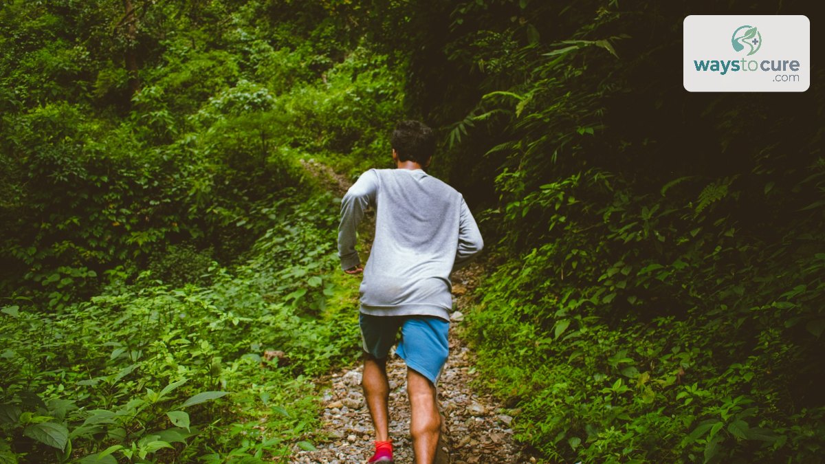 A man running away from the camera along a green forest trail